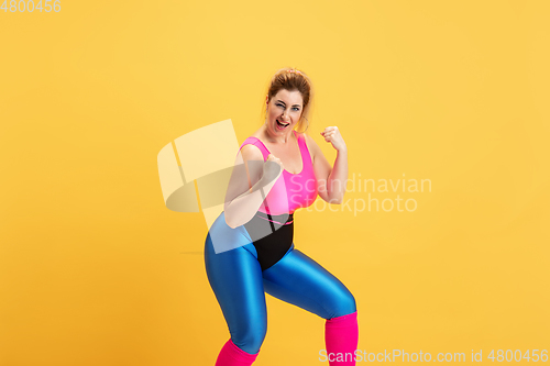 Image of Young caucasian plus size female model\'s training on yellow background