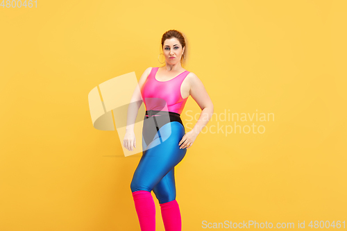 Image of Young caucasian plus size female model\'s training on yellow background