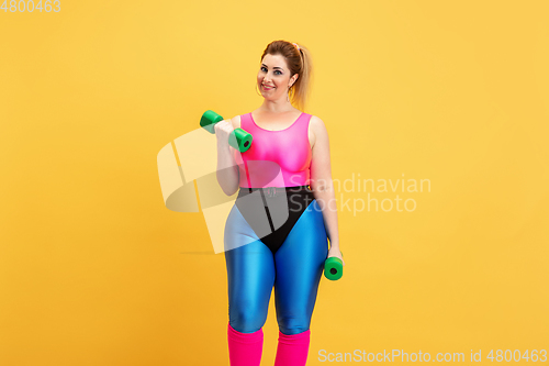 Image of Young caucasian plus size female model\'s training on yellow background