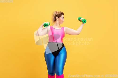 Image of Young caucasian plus size female model\'s training on yellow background