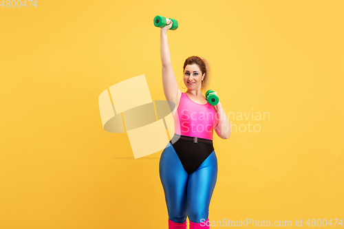 Image of Young caucasian plus size female model\'s training on yellow background
