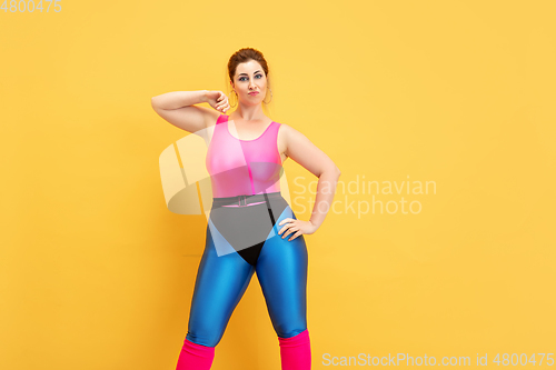 Image of Young caucasian plus size female model\'s training on yellow background