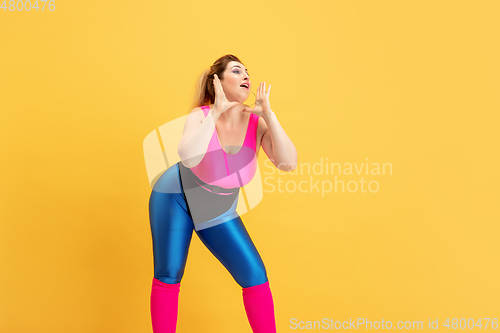 Image of Young caucasian plus size female model\'s training on yellow background