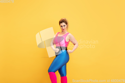 Image of Young caucasian plus size female model\'s training on yellow background