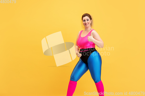 Image of Young caucasian plus size female model\'s training on yellow background