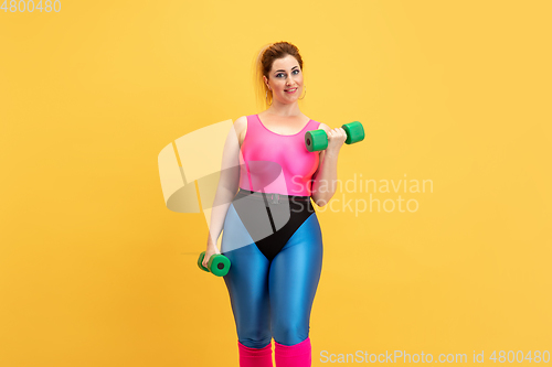 Image of Young caucasian plus size female model\'s training on yellow background