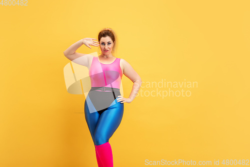 Image of Young caucasian plus size female model\'s training on yellow background