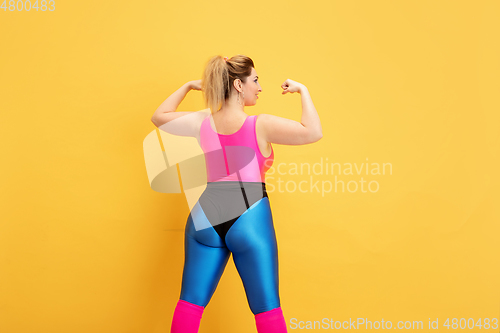 Image of Young caucasian plus size female model\'s training on yellow background