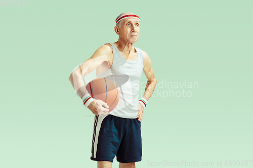 Image of Senior man playing basketball in sportwear isolated on green background