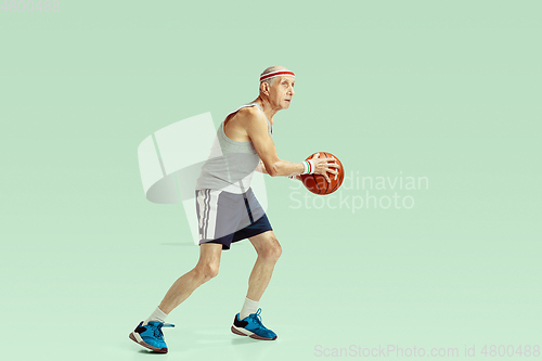 Image of Senior man playing basketball in sportwear isolated on green background