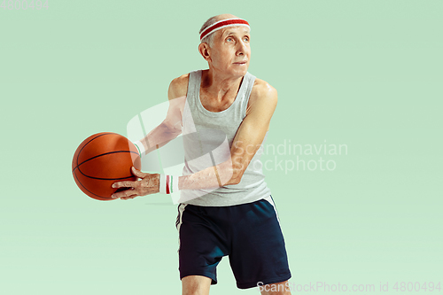 Image of Senior man playing basketball in sportwear isolated on green background