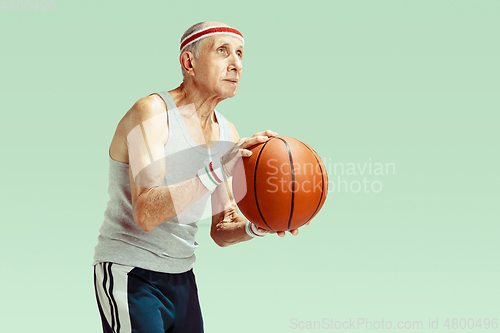 Image of Senior man playing basketball in sportwear isolated on green background