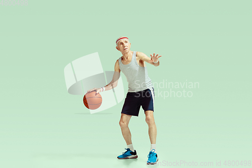 Image of Senior man playing basketball in sportwear isolated on green background