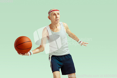 Image of Senior man playing basketball in sportwear isolated on green background