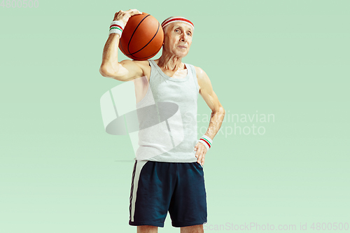 Image of Senior man playing basketball in sportwear isolated on green background