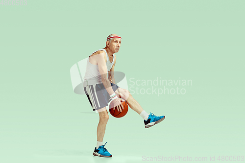 Image of Senior man playing basketball in sportwear isolated on green background