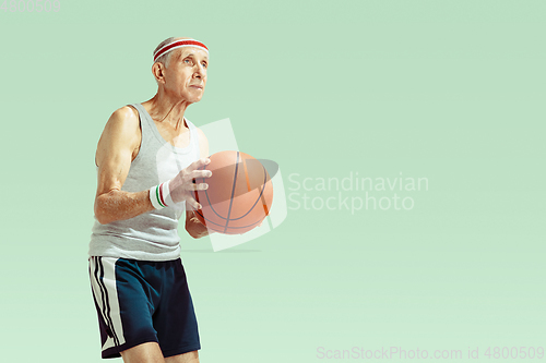 Image of Senior man playing basketball in sportwear isolated on green background