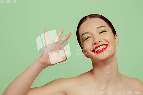 Image of Portrait of beautiful young woman with bright make-up isolated on green studio background