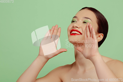 Image of Portrait of beautiful young woman with bright make-up isolated on green studio background