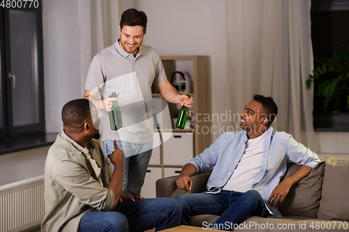 Image of happy male friends drinking beer at home at night