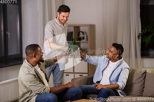 Image of happy male friends drinking beer at home at night