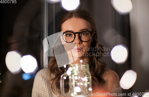 Image of woman with garland lights in glass mug at home