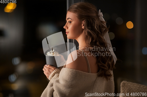 Image of woman holding mug with whipped cream at night