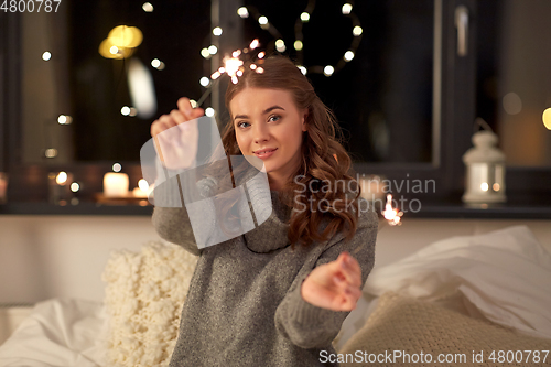 Image of happy young woman with sparklers in bed at home