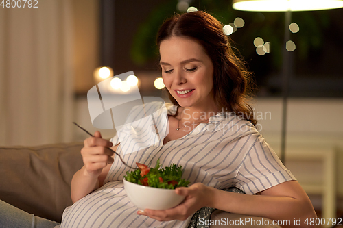 Image of happy smiling pregnant woman eating salad at home