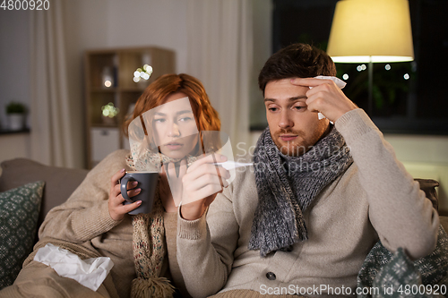 Image of sick couple with thermometer and tea at home