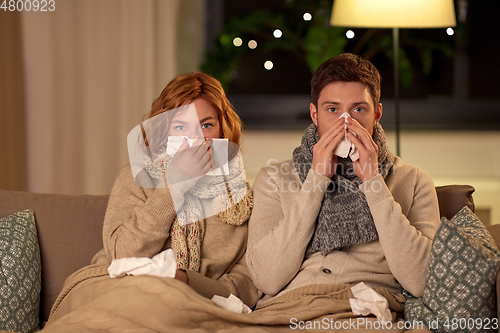 Image of sick young couple with tissue blowing nose at home