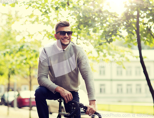 Image of young man in shades riding bicycle on city street