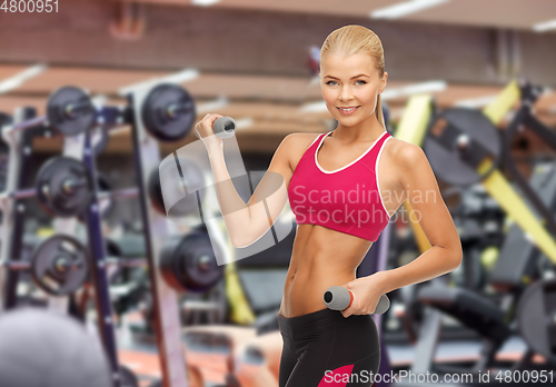 Image of happy young woman with dumbbells exercising in gym