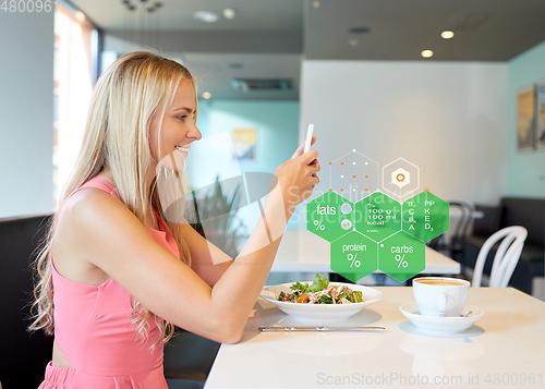 Image of happy woman with smartphone eating at restaurant