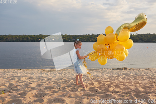 Image of Little girl with many golden balloons on the beach at sunset