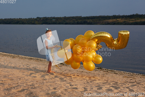 Image of Little girl with many golden balloons on the beach at sunset
