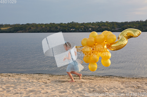 Image of Little girl with many golden balloons on the beach at sunset