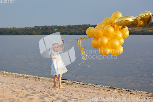 Image of Little girl with many golden balloons on the beach at sunset