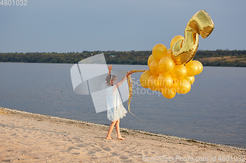 Image of Little girl with many golden balloons on the beach at sunset