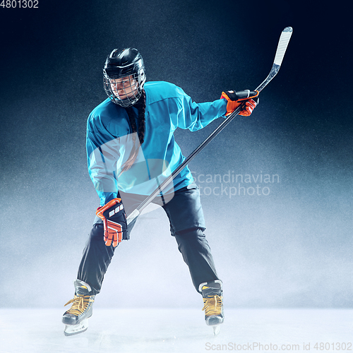 Image of Young female hockey player with the stick on ice court and blue background