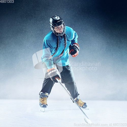 Image of Young female hockey player with the stick on ice court and blue background