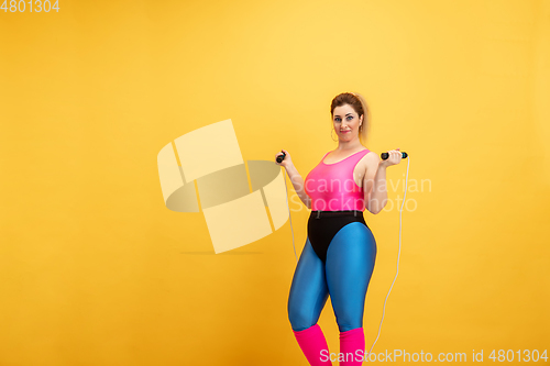 Image of Young caucasian plus size female model\'s training on yellow background