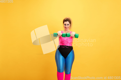 Image of Young caucasian plus size female model\'s training on yellow background