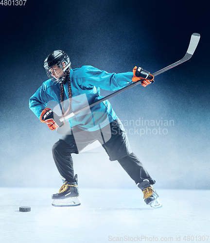 Image of Young female hockey player with the stick on ice court and blue background