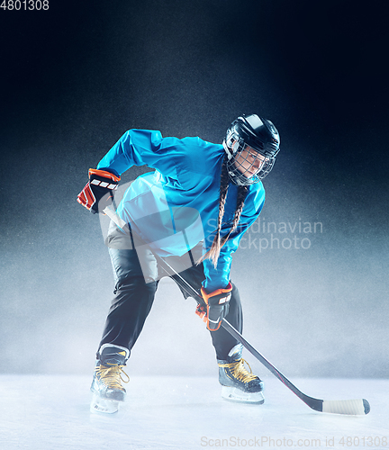 Image of Young female hockey player with the stick on ice court and blue background