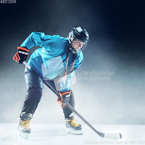 Image of Young female hockey player with the stick on ice court and blue background