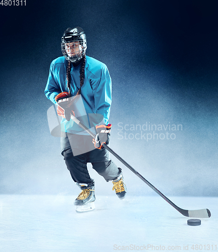 Image of Young female hockey player with the stick on ice court and blue background