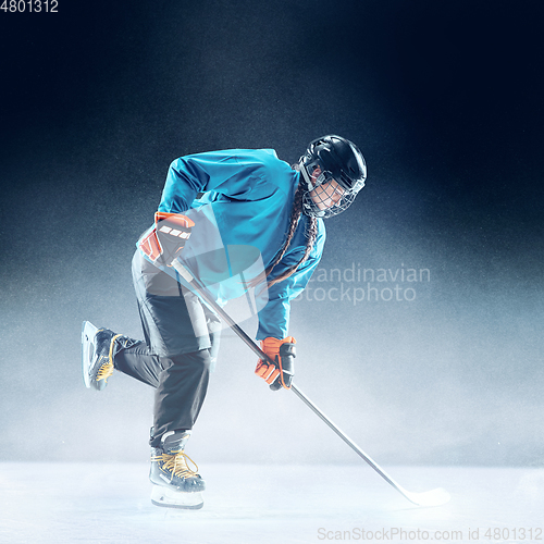 Image of Young female hockey player with the stick on ice court and blue background