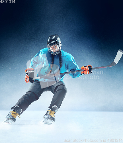Image of Young female hockey player with the stick on ice court and blue background