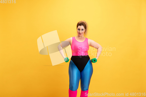 Image of Young caucasian plus size female model\'s training on yellow background